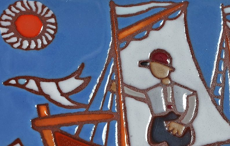 Peut inclure: Un carreau de c&eacute;ramique peint &agrave; la main repr&eacute;sentant un voilier avec une voile blanche et un personnage portant un chapeau rouge &agrave; la barre. Le carreau a un fond bleu avec un oiseau blanc volant au-dessus du bateau et un soleil rouge dans le coin sup&eacute;rieur gauche.