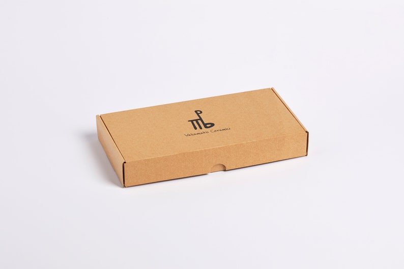 May include: A brown cardboard box with the text "Valimaki Caramels" and a logo of a stylized "MB" printed on the top.