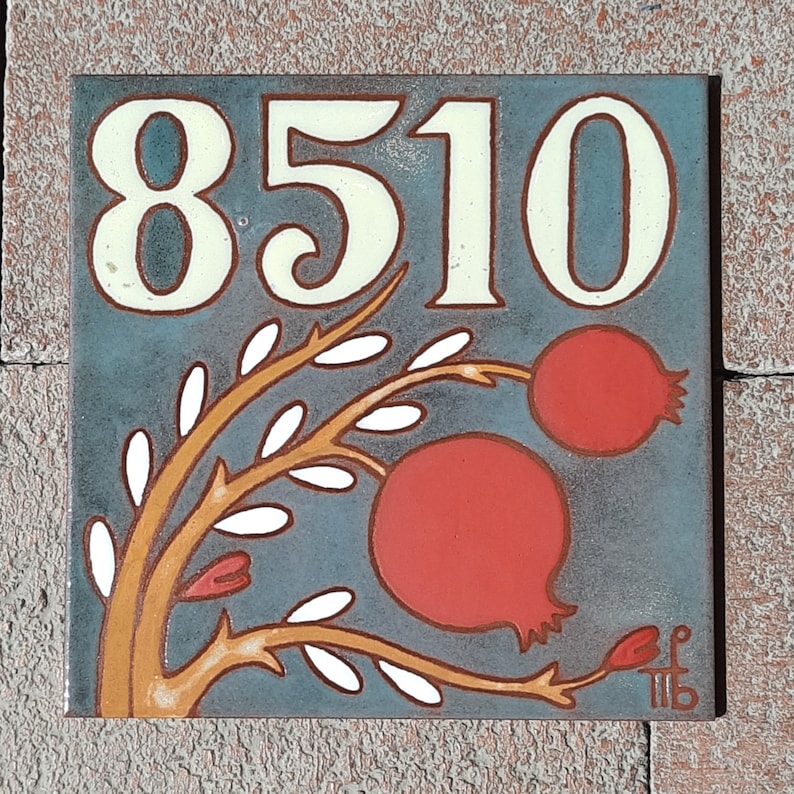 May include: A blue and white ceramic tile with the number 8510 in white lettering. The tile features a stylized orange branch with white leaves and two red pomegranates.