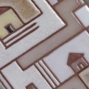 以下が含まれることがあります： 赤い屋根のスタイリッシュな家が2つある幾何学模様のセラミックタイルのクローズアップ。タイルは白で、茶色の線が引かれており、表面はテクスチャ加工されています。