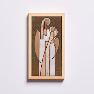 May include: A framed ceramic tile with a stylized image of two figures in white, pink, and brown against a green background. The figures are in a close embrace, with the smaller figure's head resting on the larger figure's shoulder. The tile is framed in a natural wood frame.