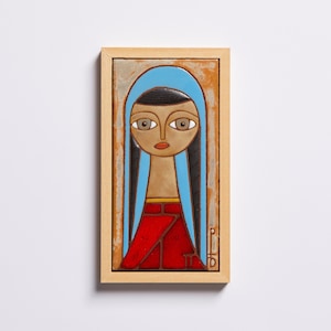 May include: A framed ceramic tile with a painting of a woman with long black hair, wearing a blue headscarf and a red dress. The woman's eyes are large and brown, and her lips are red.