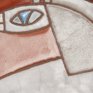 Op de afbeelding: Close-up van een keramisch bord met een gestileerd abstract ontwerp. Het bord is versierd met geometrische vormen in tinten bruin, wit en blauw.