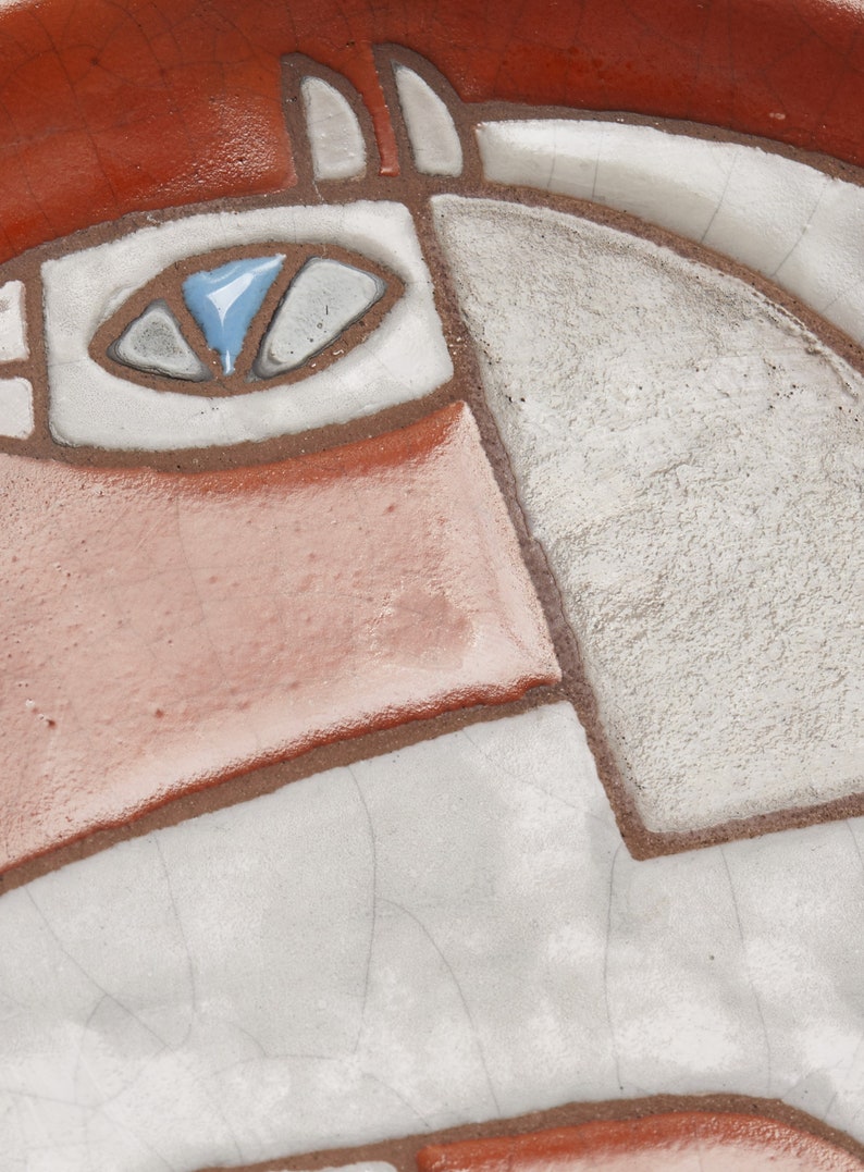 Op de afbeelding: Close-up van een keramisch bord met een gestileerd abstract ontwerp. Het bord is versierd met geometrische vormen in tinten bruin, wit en blauw.