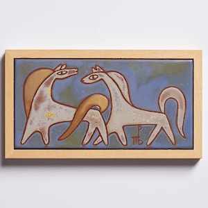 Puede incluir: Un azulejo de cerámica enmarcado con fondo azul y dos caballos blancos con contornos marrones. Los caballos se miran y tienen la cabeza inclinada. El azulejo está firmado "P.M.B."