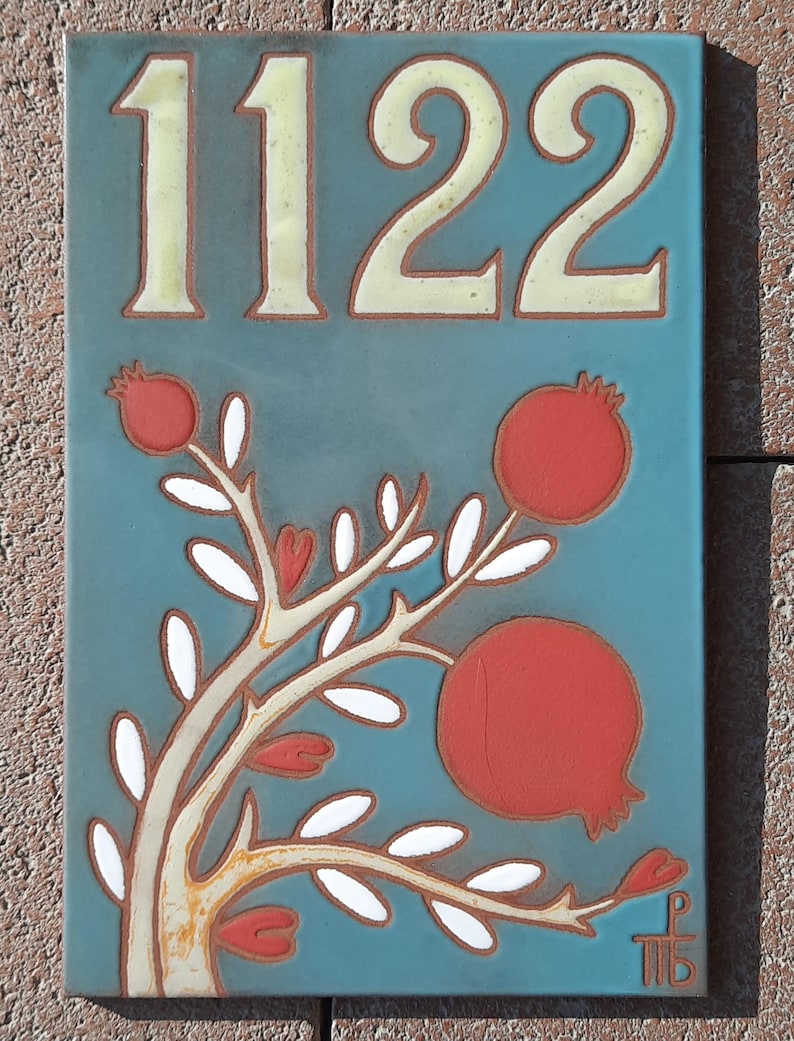 May include: A blue ceramic tile with the number 1122 in white. The tile features a stylized tree with white leaves and red pomegranates.