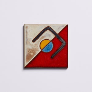 K&ouml;nnte beinhalten: Eine quadratische Keramikfliese mit geometrischem Design. Die Fliese ist diagonal in zwei Abschnitte unterteilt, einen wei&szlig;en und einen roten. Eine schwarze Linie bildet eine geschwungene Form in der Mitte der Fliese, mit einem gelben und blauen Kreis darin.