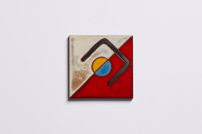 K&ouml;nnte beinhalten: Eine quadratische Keramikfliese mit geometrischem Design. Die Fliese ist diagonal in zwei Abschnitte unterteilt, einen wei&szlig;en und einen roten. Eine schwarze Linie bildet eine geschwungene Form in der Mitte der Fliese, mit einem gelben und blauen Kreis darin.