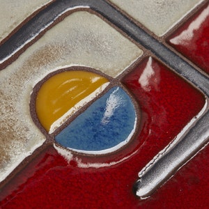 K&ouml;nnte beinhalten: Nahaufnahme einer Keramikfliese mit geometrischem Muster. Die Fliese ist in den Farben Gelb, Blau und Rot gehalten. Die Fliese hat eine gl&auml;nzende Oberfl&auml;che.