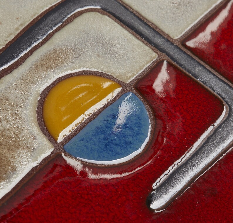 K&ouml;nnte beinhalten: Nahaufnahme einer Keramikfliese mit geometrischem Muster. Die Fliese ist in den Farben Gelb, Blau und Rot gehalten. Die Fliese hat eine gl&auml;nzende Oberfl&auml;che.