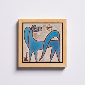 Puede incluir: Azulejo enmarcado con una ilustración de caballo azul estilizado. El caballo tiene un cuello y una cola largos, con contornos marrones. Un pequeño diseño de estrella está encima del caballo. El azulejo está enmarcado en un marco de madera natural.