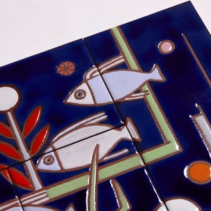 May include: A set of blue ceramic tiles with a stylized design of fish, plants, and geometric shapes. The tiles are decorated with white, red, orange, and green paint.