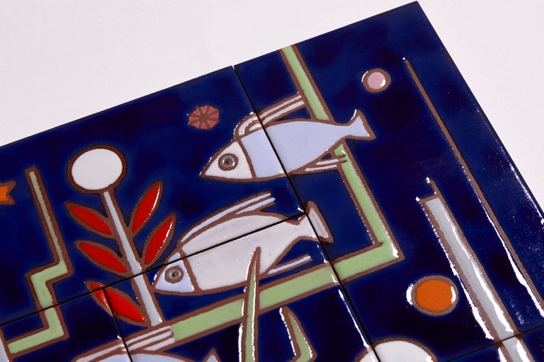 May include: A set of blue ceramic tiles with a stylized design of fish, plants, and geometric shapes. The tiles are decorated with white, red, orange, and green paint.