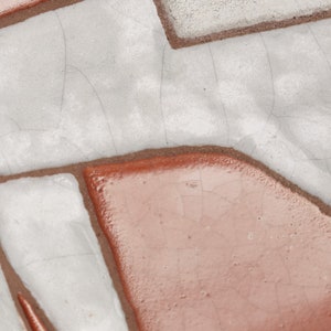 Op de afbeelding: Een witte keramische tegel met een gestileerd beeld van een hert in een bruine glazuur. Het hert is wit omrand en heeft een eenvoudig, geometrisch ontwerp.