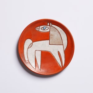Op de afbeelding: Een wit keramiek bord met een gestileerd oranje paardenontwerp. Het paard heeft een blauw oog en is zwart omrand.