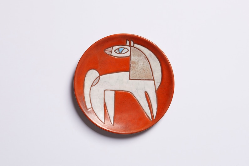 Op de afbeelding: Een wit keramiek bord met een gestileerd oranje paardenontwerp. Het paard heeft een blauw oog en is zwart omrand.