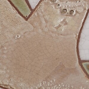 May include: Close-up of a ceramic tile with a crackled glaze. The tile has a light brown background with a pattern of green and brown lines. The lines create a design that resembles a tree branch.