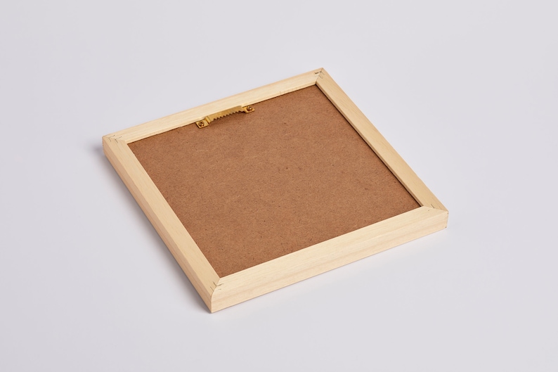 May include: A wooden picture frame with a brown cardboard backing. The frame has a gold-colored hanging hook on the back.