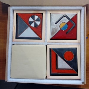 May include: Four ceramic tiles with geometric designs in a wooden box. The tiles feature black, white, red, and blue colors. The designs include a circle with a smaller circle inside, a curved line, a triangle, and a circle.