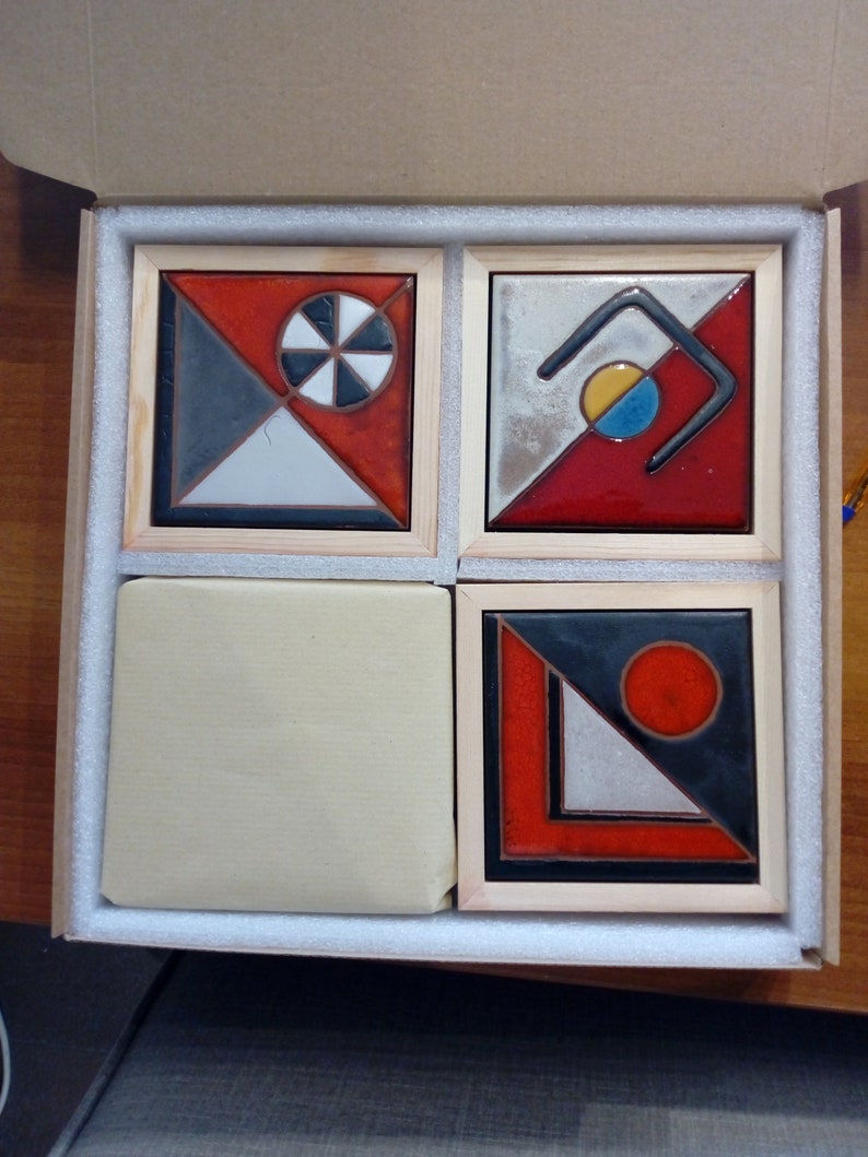 May include: Four ceramic tiles with geometric designs in a wooden box. The tiles feature black, white, red, and blue colors. The designs include a circle with a smaller circle inside, a curved line, a triangle, and a circle.