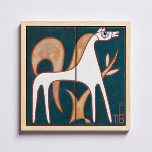 Puede incluir: Un azulejo de cerámica enmarcado con un caballo blanco estilizado de pie junto a un árbol marrón sobre un fondo azul verdoso. El caballo tiene un ojo azul y el azulejo está firmado "MB" en la esquina inferior derecha.