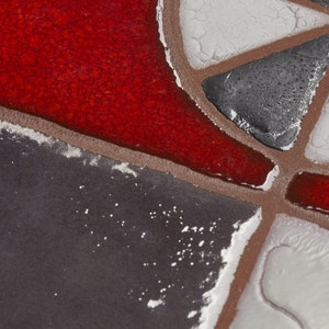 May include: Close-up of a mosaic tile with red, white, and gray geometric shapes. The tile has a textured surface and a slightly worn appearance.