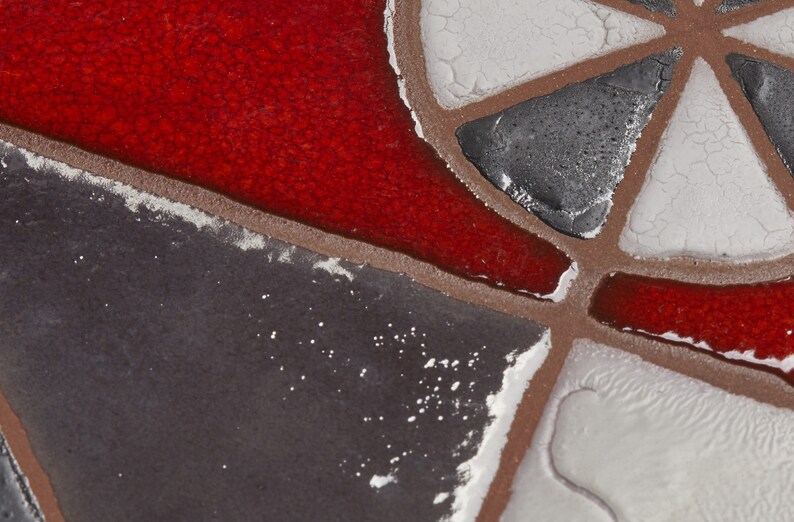 May include: Close-up of a mosaic tile with red, white, and gray geometric shapes. The tile has a textured surface and a slightly worn appearance.