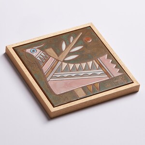 May include: A framed ceramic tile with a stylized pink bird with geometric patterns and a green branch with leaves on a brown background.