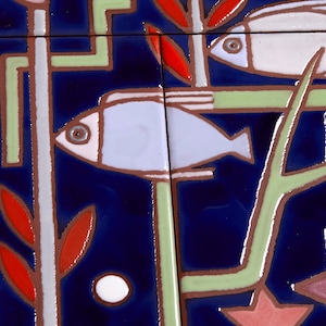 May include: A close-up of a blue and white ceramic tile with a stylized design of two fish swimming among red and green plants. The tile has a textured surface and a glossy finish.