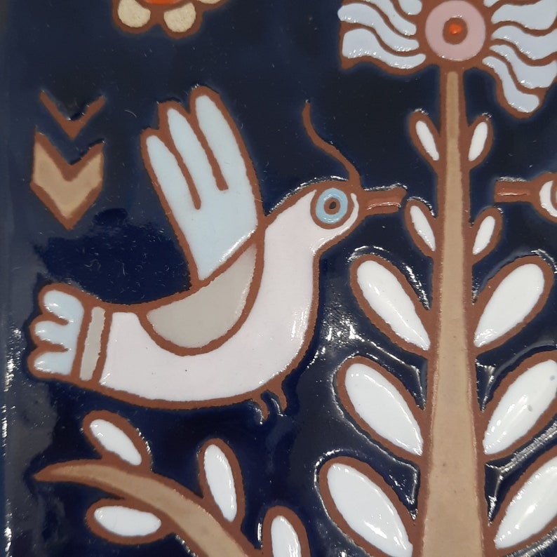 May include: A white bird with blue accents flies over a brown branch with white leaves against a dark blue background. The bird has a blue eye and a long beak.