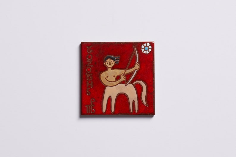 Może przedstawiać: Czerwona płytka ceramiczna z białą i złotą ilustracją centaura trzymającego łuk i strzałę. Płytka ma napis "SAGITTARIUS" napisany pionowo po lewej stronie i symbol Strzelca w lewym dolnym rogu.