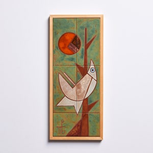Könnte beinhalten: Ein gerahmtes Keramikfliesenkunstwerk, das einen stilisierten weißen Vogel mit blauem Auge darstellt, der auf einem braunen Ast sitzt, vor einem grünen Hintergrund mit einer roten und orangefarbenen Sonne.