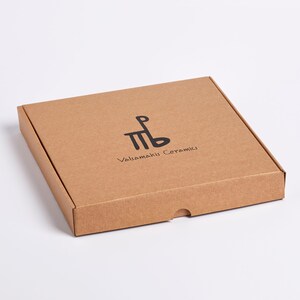 May include: A square, brown cardboard box with a lid. The box has a black logo and text that reads "Valiamaki Ceramics". The box is on a white background.