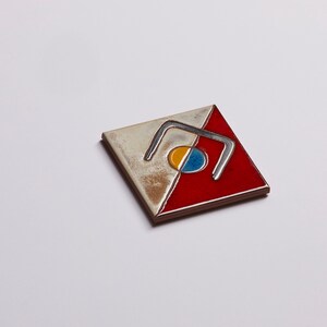 K&ouml;nnte beinhalten: Eine quadratische Keramikfliese mit einem rot-wei&szlig;-blauen Design. Die Fliese zeigt eine stilisierte geometrische Form mit einem Kreis in der Mitte.