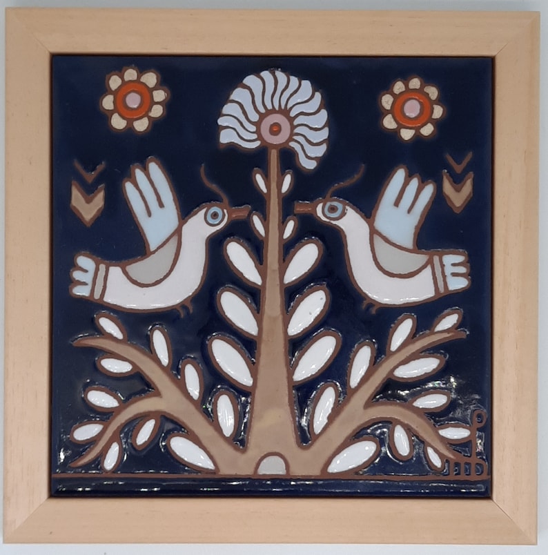 May include: A ceramic tile with a blue background features two white birds perched on a brown tree with white leaves. The tree has a white flower with a pink center. There are three white circles with orange and pink centers on the tile.