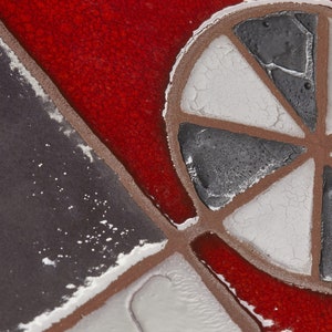 May include: Close-up of a red, white, and gray mosaic tile with a geometric design. The tile features a circular pattern with six spokes radiating from the center.