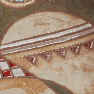Op de afbeelding: Close-up van een keramisch bord met een decoratief ontwerp. Het bord heeft een geometrisch patroon met witte, bruine en rode accenten. Het ontwerp doet denken aan Native American art.