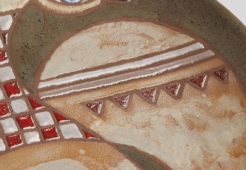 Op de afbeelding: Close-up van een keramisch bord met een decoratief ontwerp. Het bord heeft een geometrisch patroon met witte, bruine en rode accenten. Het ontwerp doet denken aan Native American art.