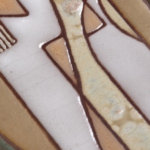 May include: Close-up of a ceramic tile with a geometric design in shades of brown, beige, and white. The tile has a textured surface and a glossy finish.