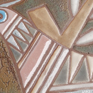 May include: A ceramic tile with a stylized bird design in shades of brown, pink, white, and blue. The bird is perched on a branch with leaves. The tile has a textured surface.
