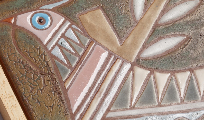 May include: A ceramic tile with a stylized bird design in shades of brown, pink, white, and blue. The bird is perched on a branch with leaves. The tile has a textured surface.