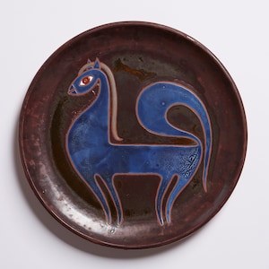 Puede incluir: Un plato de cerámica marrón con un diseño de animal estilizado azul. El animal tiene una cola larga y un ojo rojo.
