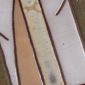 May include: Close-up of a ceramic tile with a brown, white, and beige design. The tile has a textured surface and a crackled glaze.