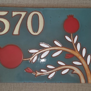 May include: A blue ceramic tile with the number 570 in white and a stylized red pomegranate branch with white leaves.