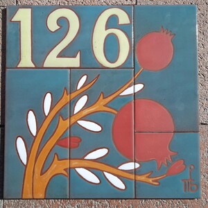 May include: A blue and orange ceramic tile with the number 126 in yellow lettering. The tile features a stylized pomegranate tree with red pomegranates and white leaves.