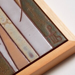 May include: A framed ceramic tile with a geometric design in shades of brown, green, and white. The tile is signed with a stylized letter "P" in the lower right corner.