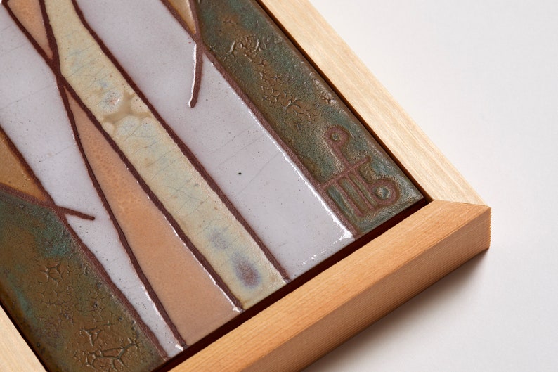 May include: A framed ceramic tile with a geometric design in shades of brown, green, and white. The tile is signed with a stylized letter "P" in the lower right corner.