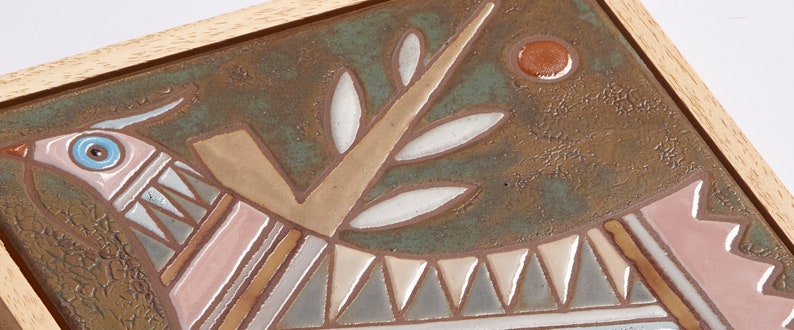 May include: A ceramic tile with a stylized bird design. The bird is pink, brown, and blue with a white eye. The background is a mottled green with a brown circle.