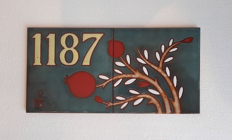 May include: Two blue ceramic tiles with a white background. The left tile has the number 1187 in yellow lettering. The right tile has a stylized tree with white leaves and red fruit.