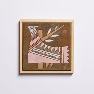 May include: A framed ceramic tile with a stylized pink bird with geometric patterns and a white branch with leaves on a brown background.